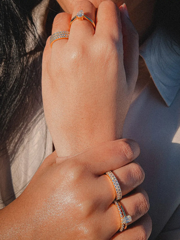 Diamantsmykker på ei dame, med en pæreformet diamantring, en stacka diamantring og en radiant-slipt diamant forlovelsesring. På venstre handa har a på seg en giftering.