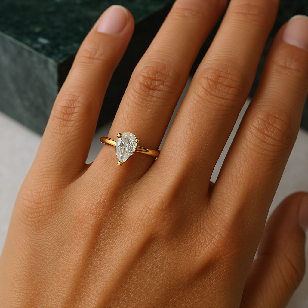 Onyx Oslo Pæreslipt Exo Diamantring på en hånd, med en 1 karat VVS1 pæreslipt stein i 18K gull, mot en grønn marmorbakgrunn